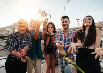 Group of happy young people throwing confetti while enjoying rooftop party. Friends having fun at terrace party.